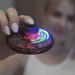 Flynova Mini UFO Spinner toy with colorful LED lights and spinning design, held in hand against a white background.
